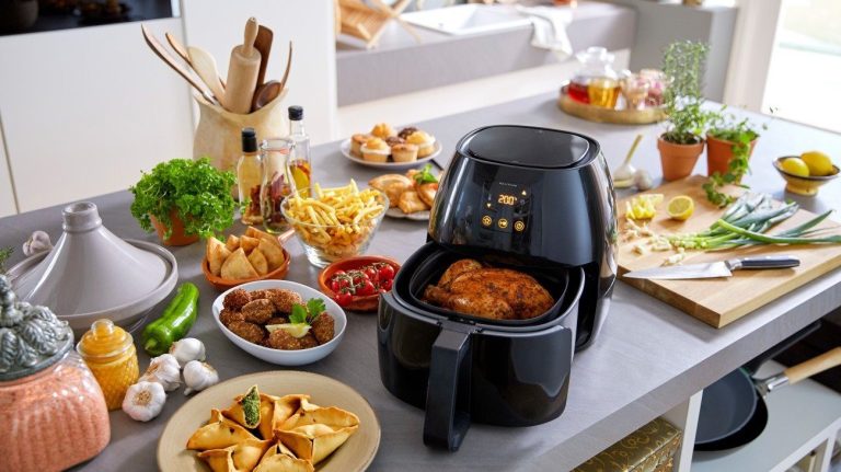 An air fryer on a table surrounded by delicious fried food