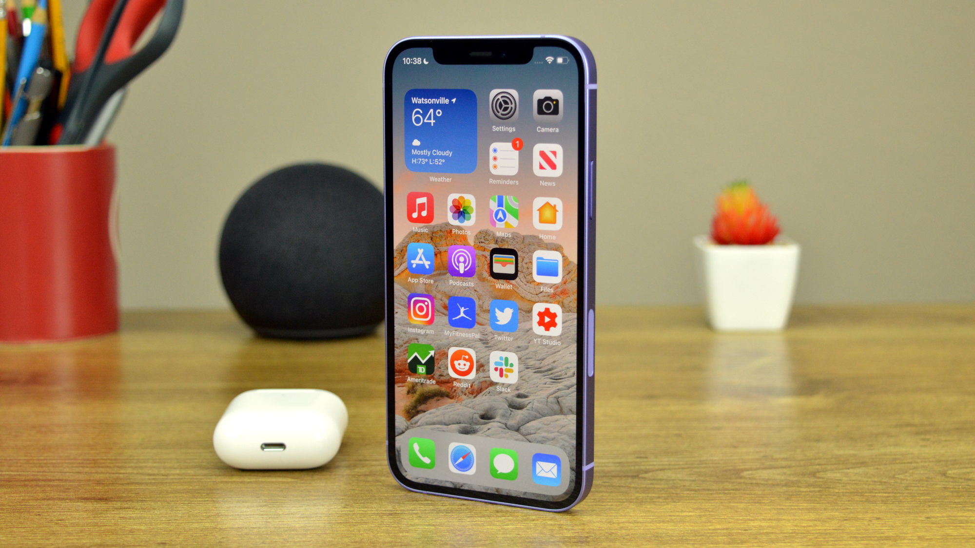 Apple iPhone 12 on a desk next to AirPods and an Amazon Echo Dot