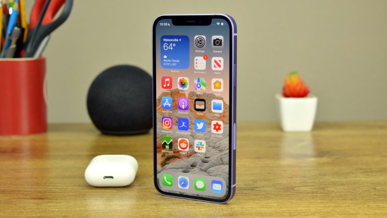 Apple iPhone 12 on a desk next to AirPods and an Amazon Echo Dot