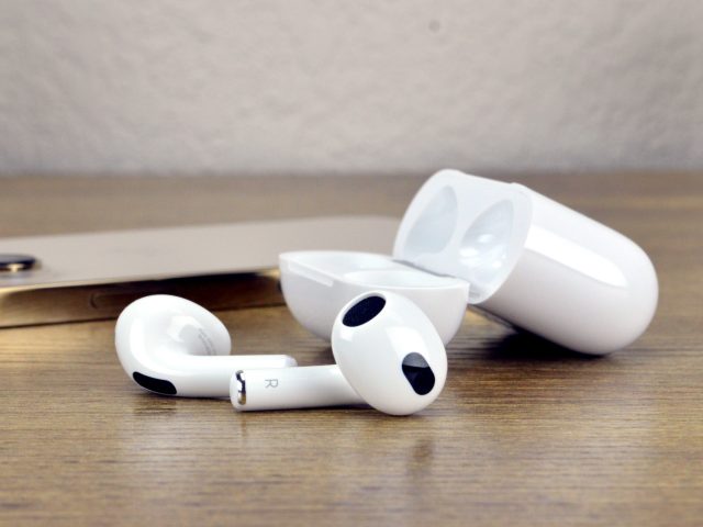 Apple AirPods 3 on a table next to an iPhone 13 Pro