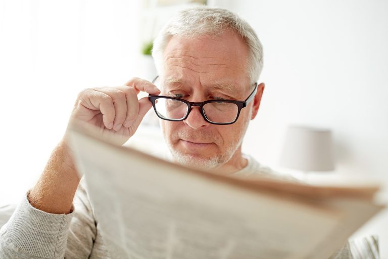 Senior man in glasses reading newspaper at home