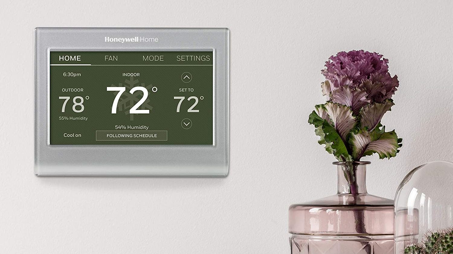 A thermostat on a wall next to a flower vase.