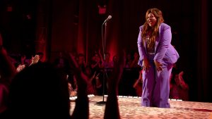 Nicole Byer woman in purple suit at microphone