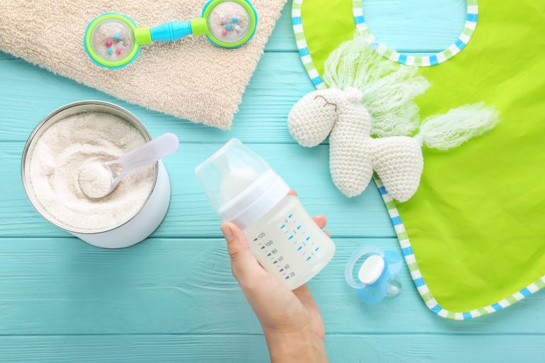 Woman holding feeding bottle of baby milk formula on wooden background
