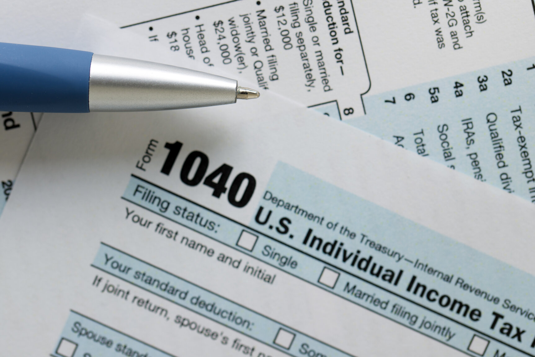 An IRS 1040 income tax form is shown with a blue pen