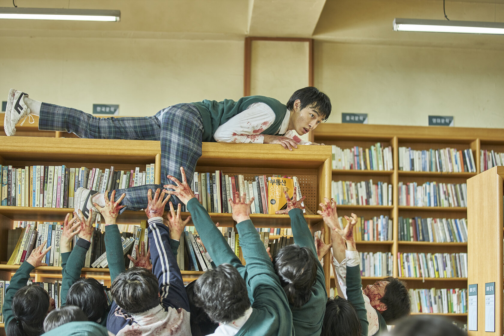 A student flees in a library from zombies below