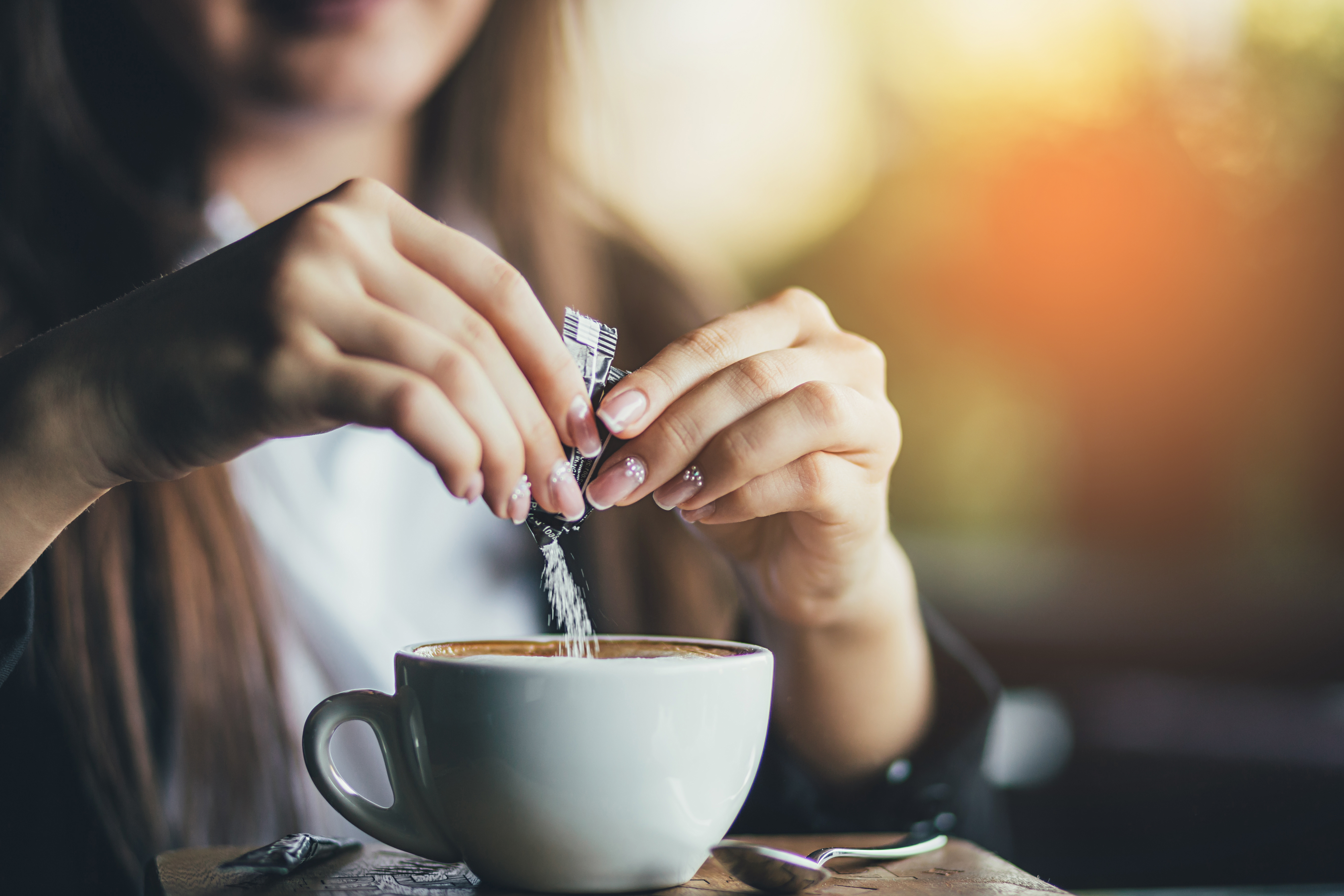 Female hand pours sugar into coffee 