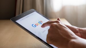 A person's hand is tapping on a tablet with Google on screen
