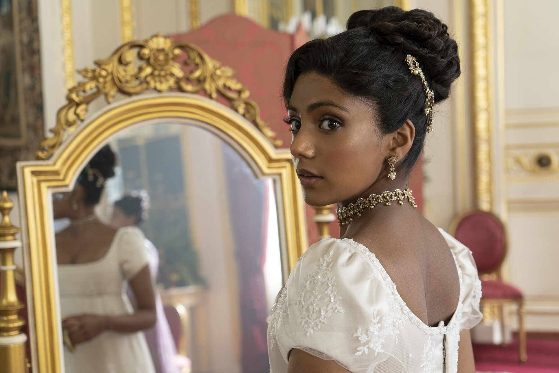 young woman wearing a dress stands in front of a mirror