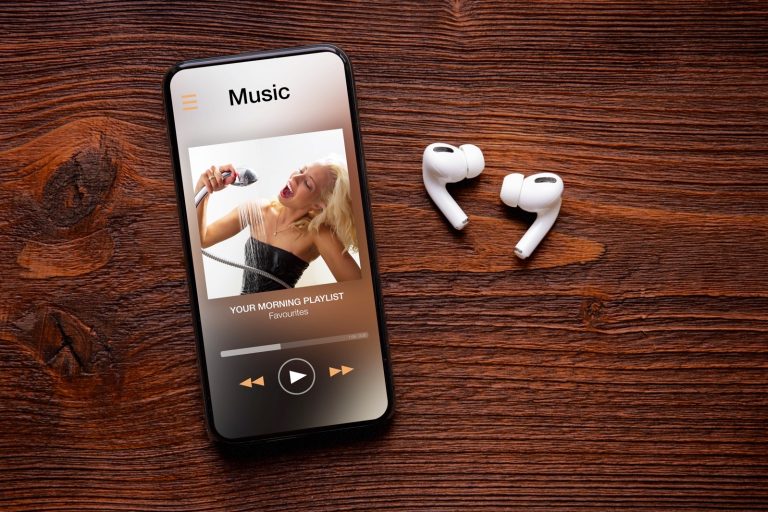 Music player on screen of iPhone and AirPods Pro on wooden surface.