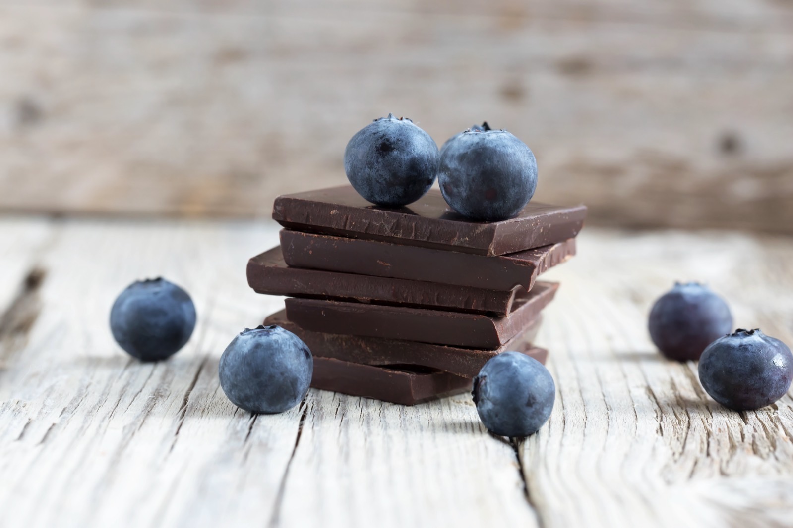 Dark chocolate stack and fresh organic blueberries on wooden table.