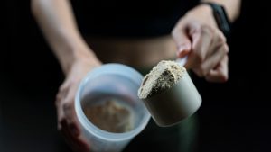 Close up of a person with measuring scoop of whey protein and shaker bottle, preparing protein shake.