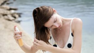 Woman applying sunscreen spray on her hair at the beach.