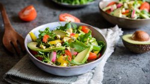 Healthy raw arugula salad with avocado, radish, bell pepper, tomato and Roquefort cheese.