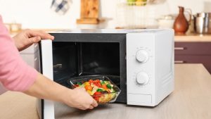 A person putting a bowl with vegetables in the microwave.