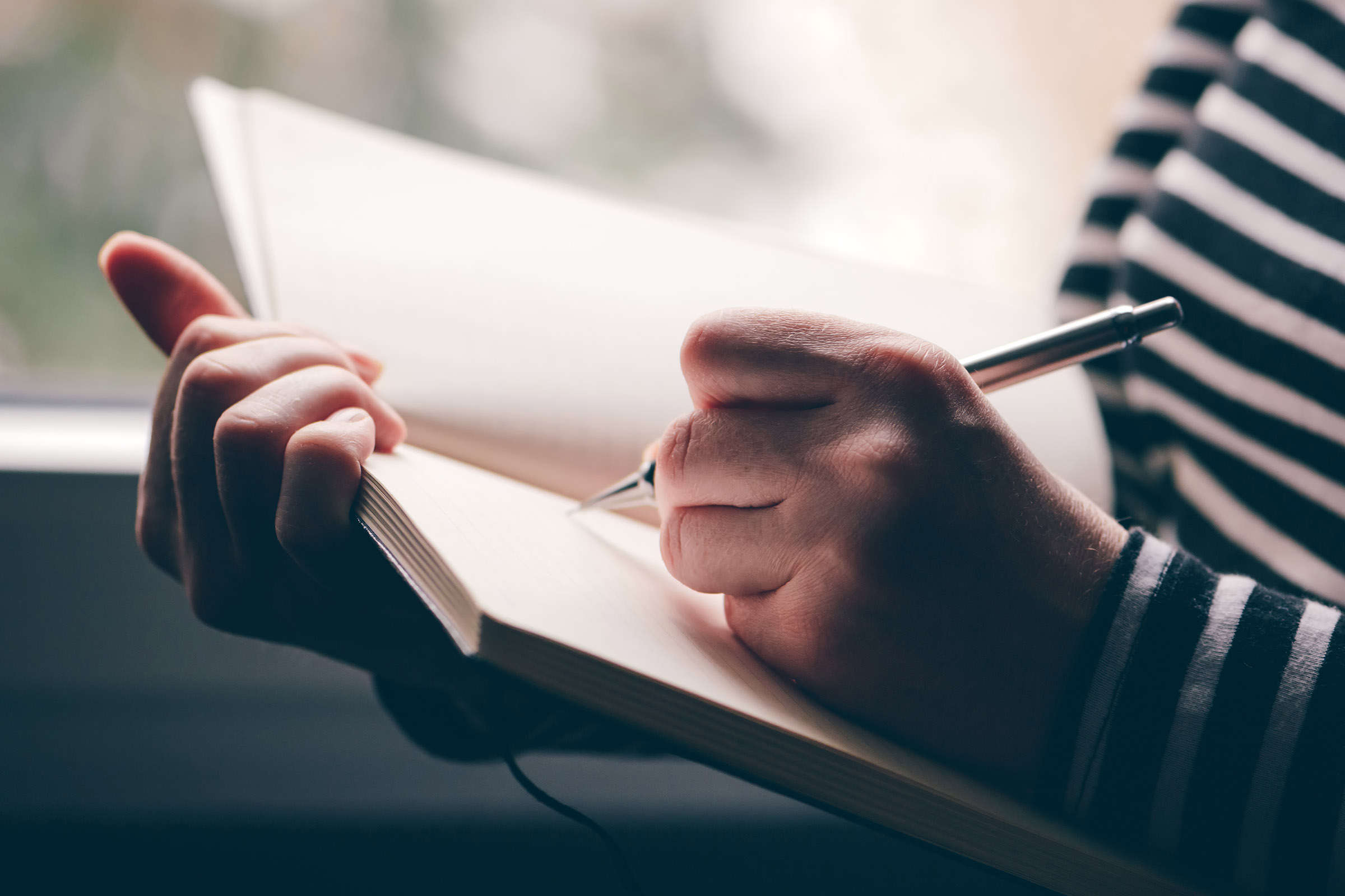 left-handed person writing in journal