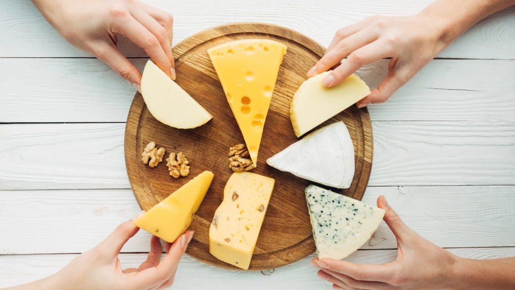 People choosing various types of cheese products from a platform.