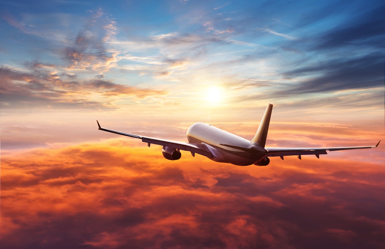 Commercial airplane flying above clouds in sunset light.