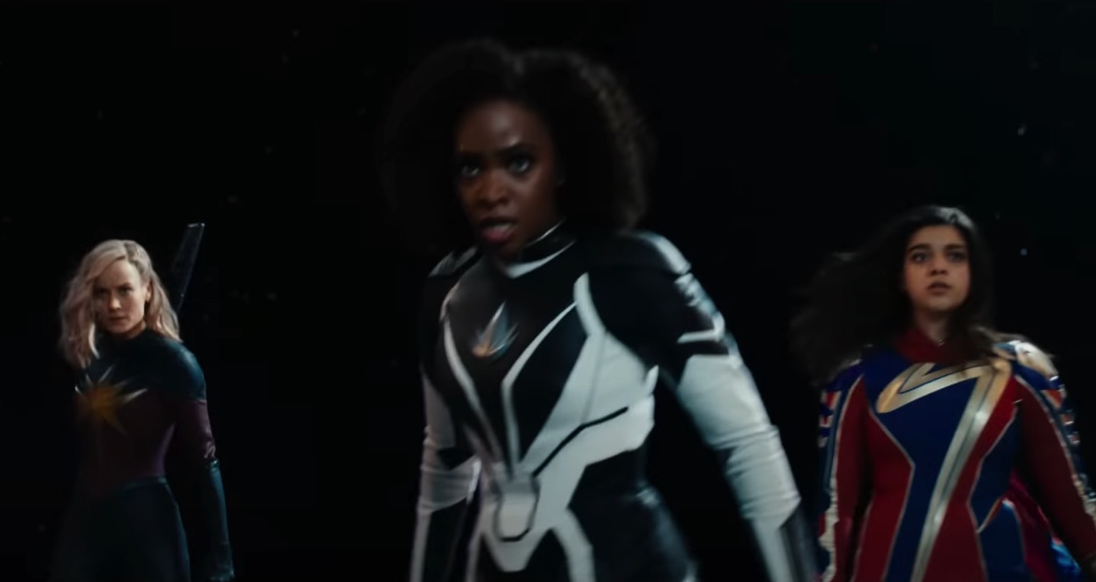 Carol Danvers (Brie Larson), Monica Rambeau (Teyonah Parris), and Kamala Khan (Iman Vellani) in superhero costumes in The Marvels trailer 1.